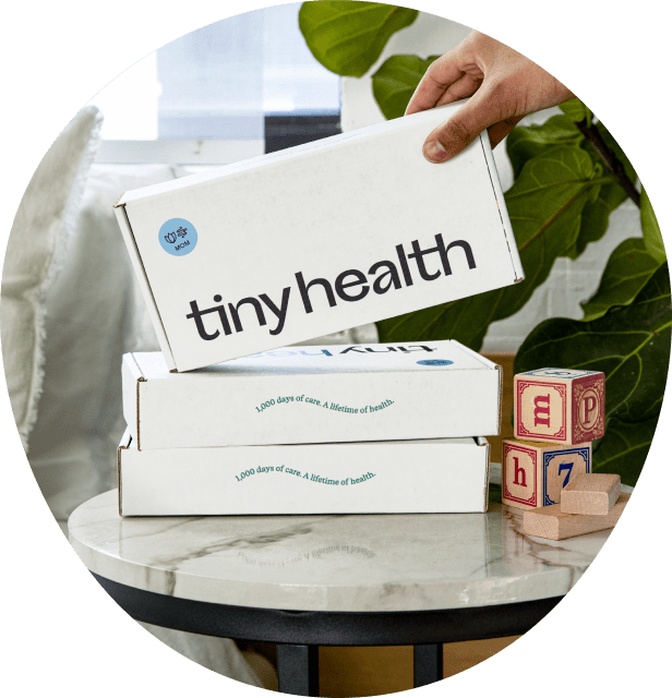 A picture with a stack of Tiny Health gut health test kits for pregnancy on top of a coffee table, and a hand reaching for the top one