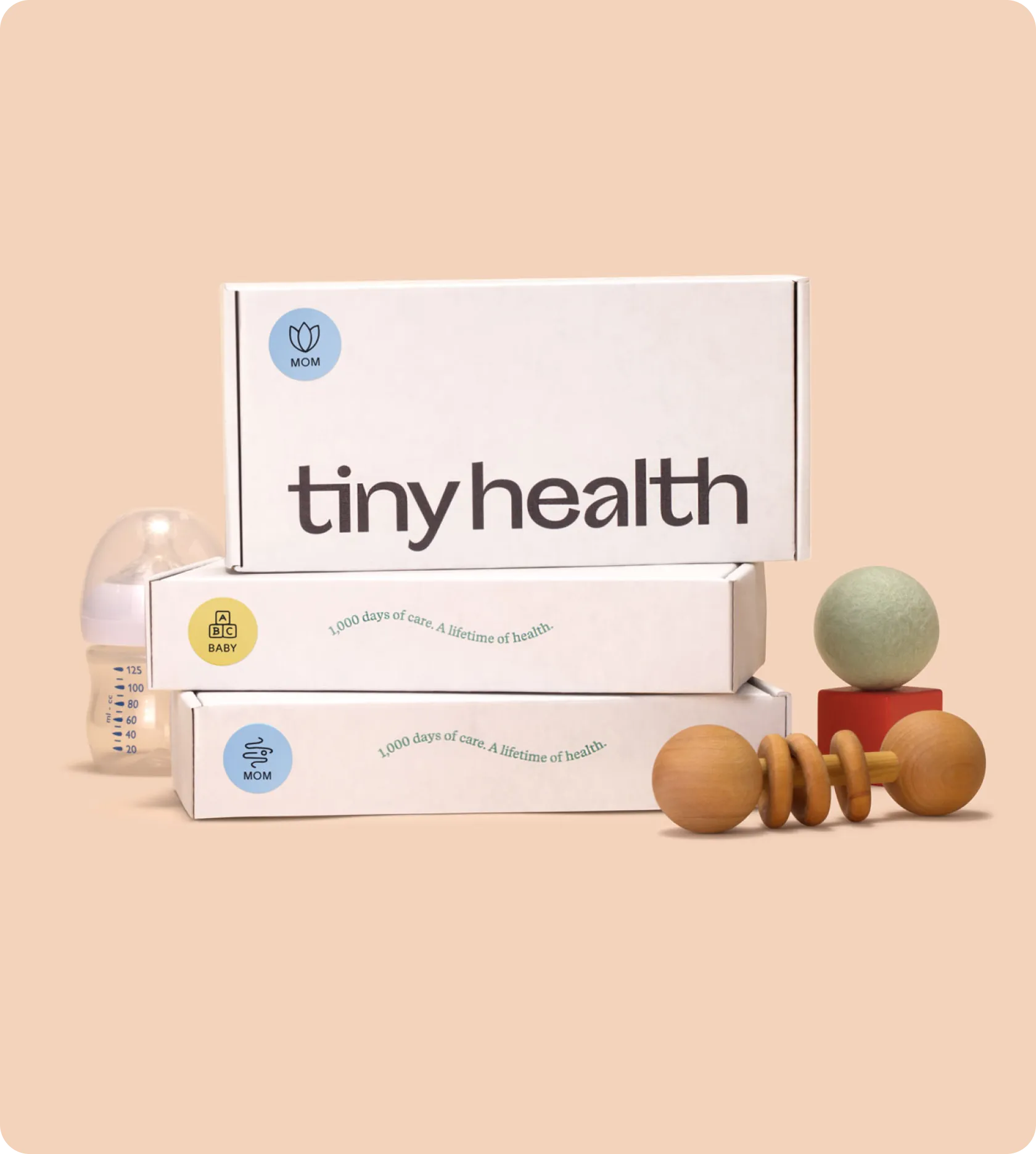 Stack of Tiny Health boxes with a slogan, a baby bottle, and wooden toys.