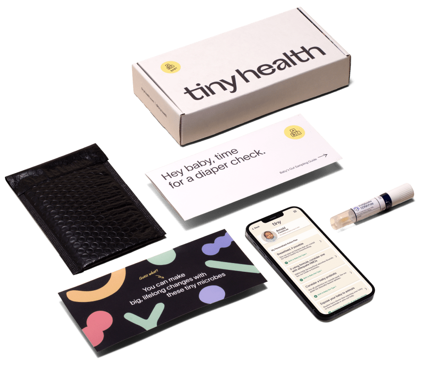 A gut health test kit laid out on a flat surface including a test box, an envelope, an instruction manual, a test swab and a phone with Tiny Health's mobile app