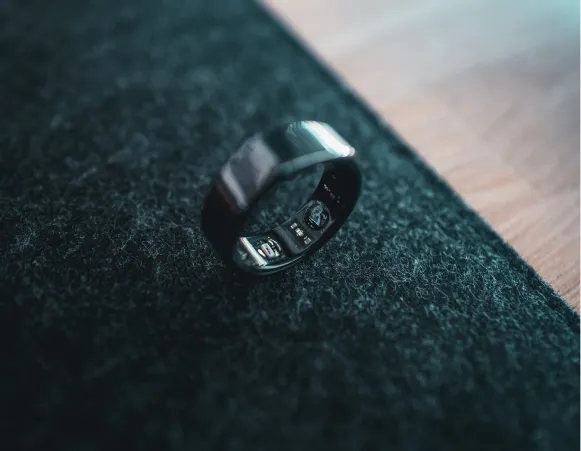 A close-up of a sleek black ring resting on a textured surface, with a wooden background partially visible.