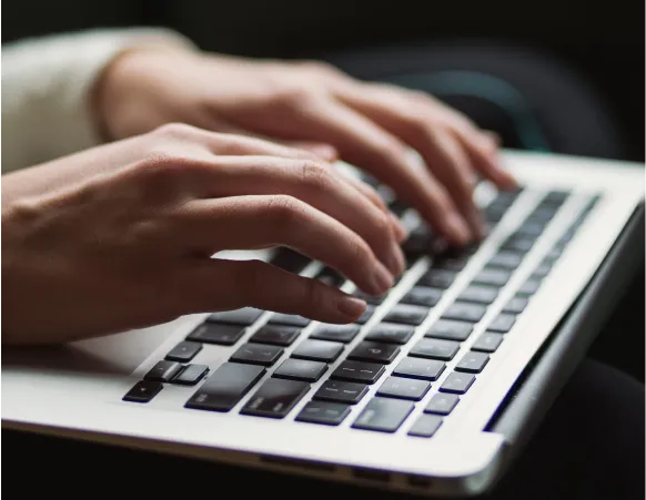 Close-up of hands typing on a laptop keyboard, with fingers positioned over the keys.