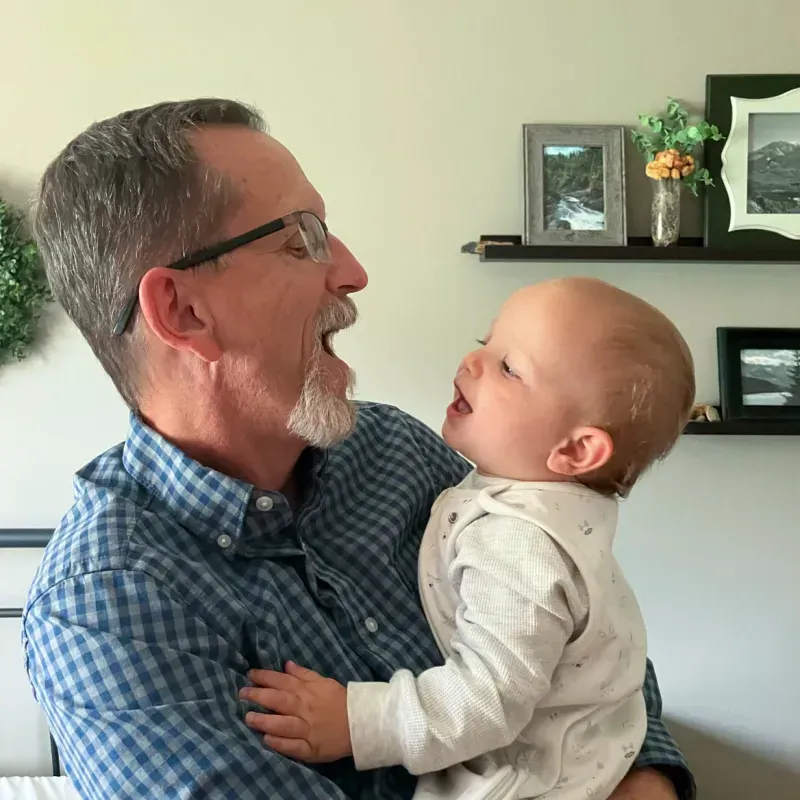 An older man and a baby are smiling at each other, engaged in a joyful interaction.