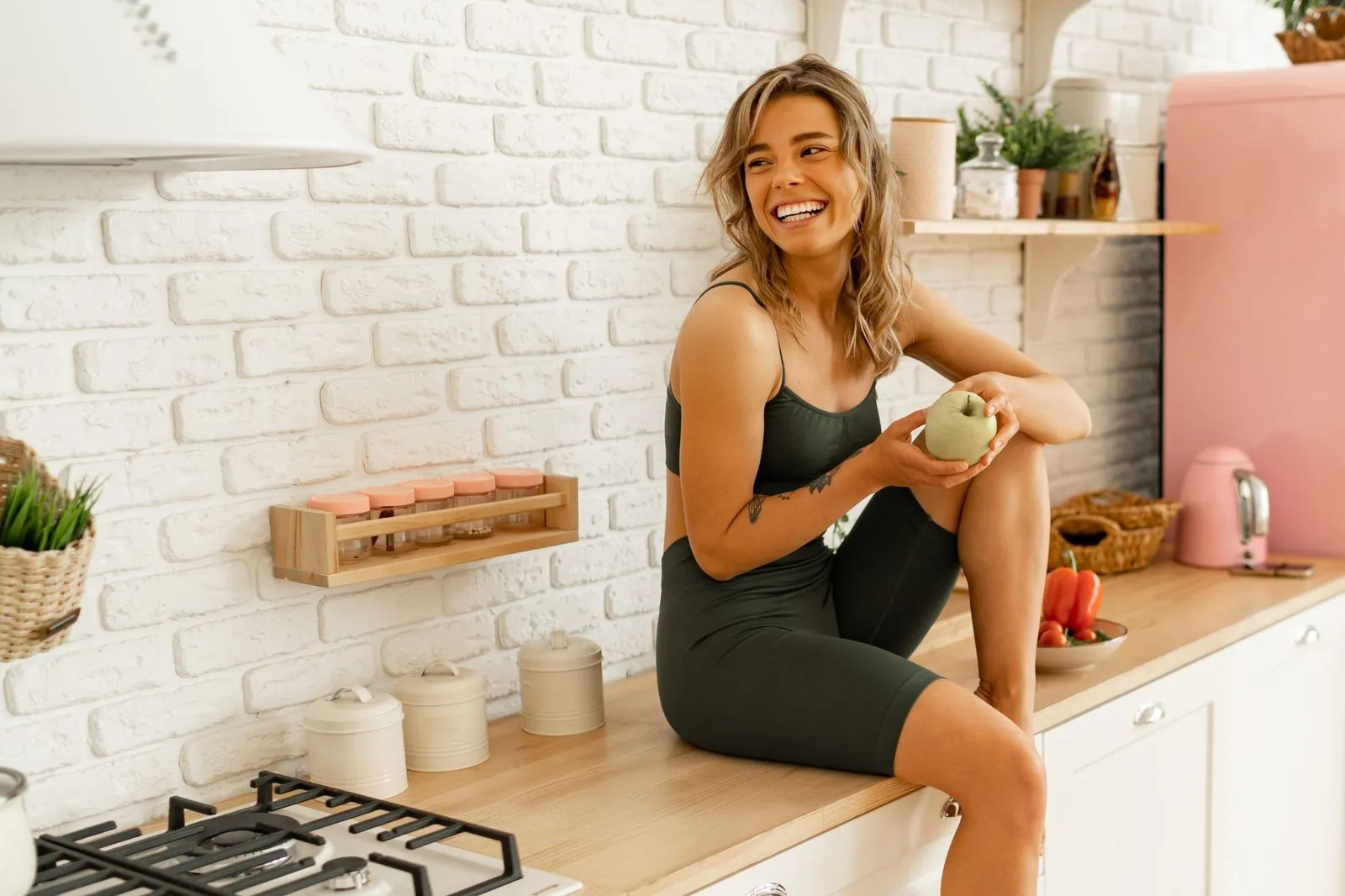 A woman sitting in a modern kitchen countertop holding an apple.
