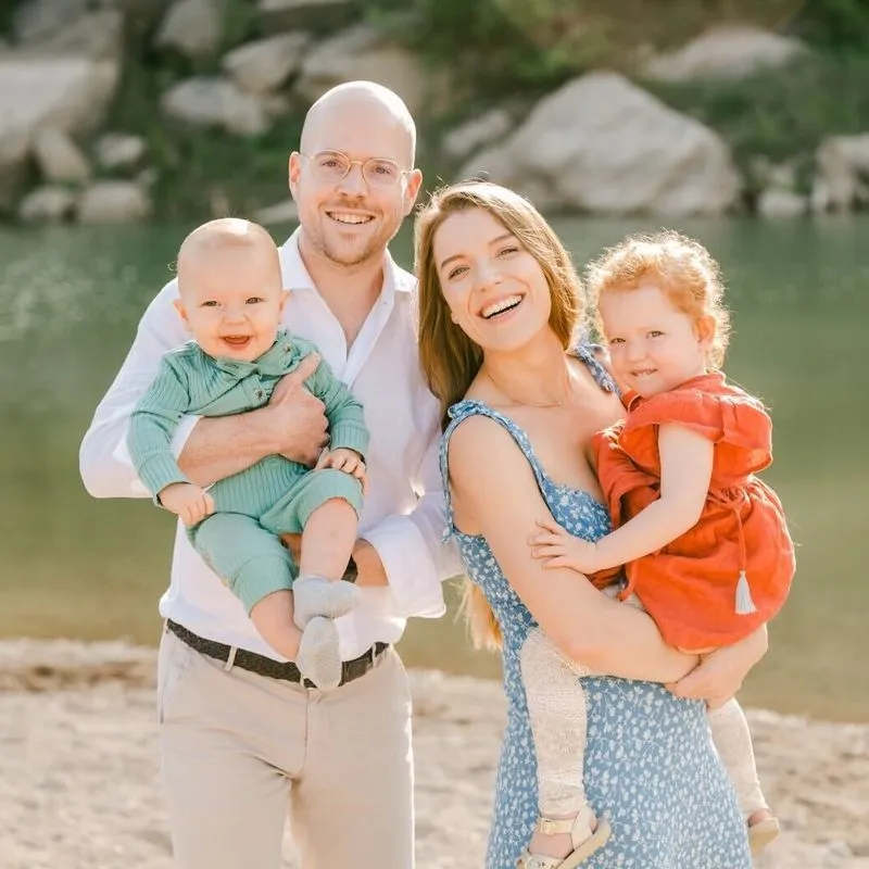 a family of 4 smiling to camera, a dad with his baby in his hands, and a mom with her toddler in her hands