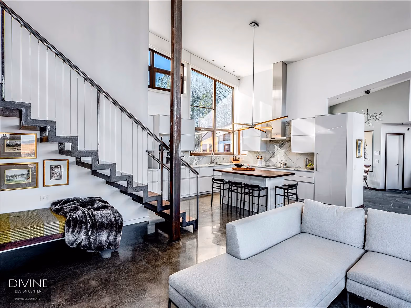 Living area with a dark metal staircase, a gray sectional sofa with a fringed throw blanket, tall wood-framed windows, framed art on the wall, and polished concrete flooring