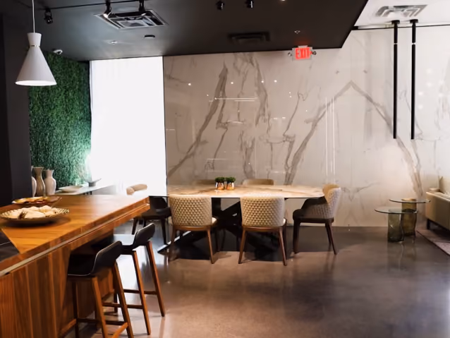 Modern dining area with wood bar stools, a table with chairs, and a marble wall background.