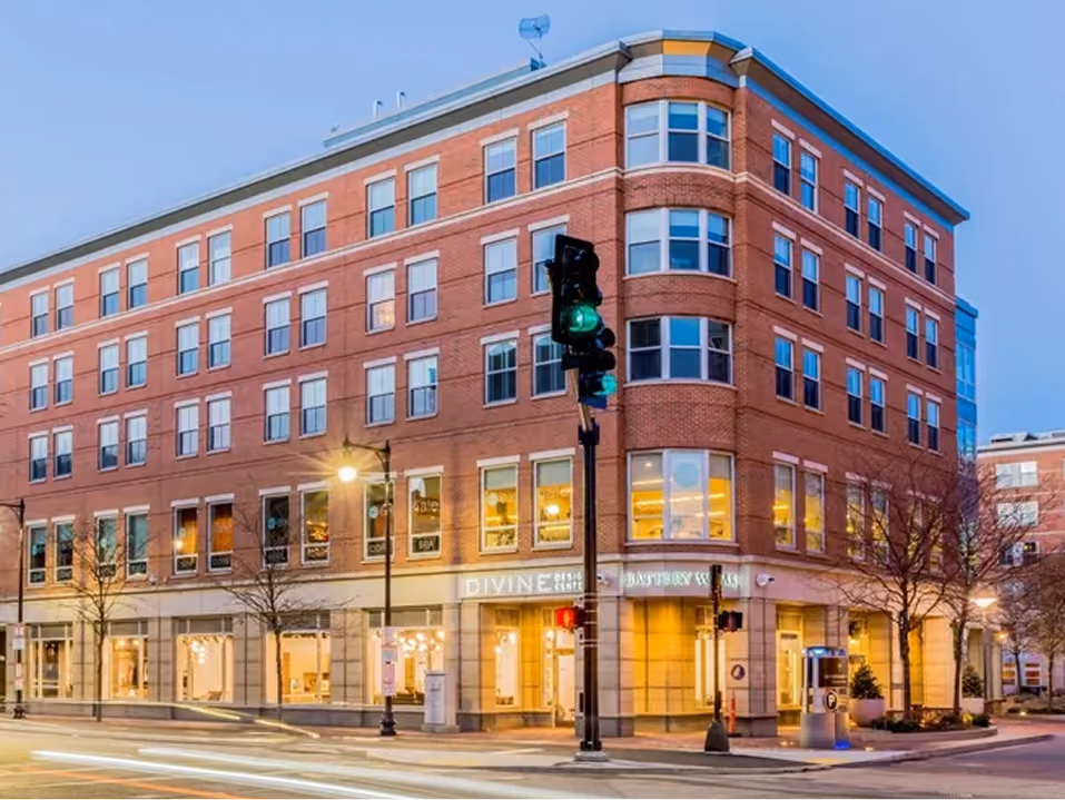 Four-story brick building on a street corner with lit windows and a green traffic light.