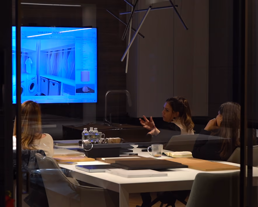 Three people in a dark conference room discussing an interior design plan shown on a bright screen.
