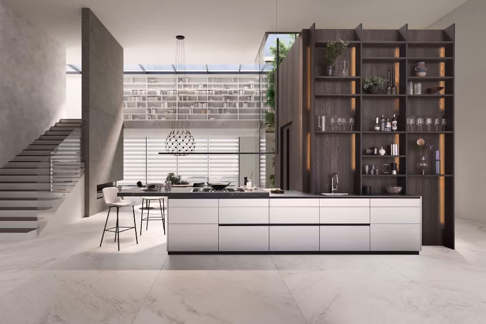 Modern minimalist kitchen with a large white island countertop featuring a built-in stove, two tall stools, and a dark wood open shelving unit stocked with glassware and plants, set in a spacious room with marble flooring and floating staircase.