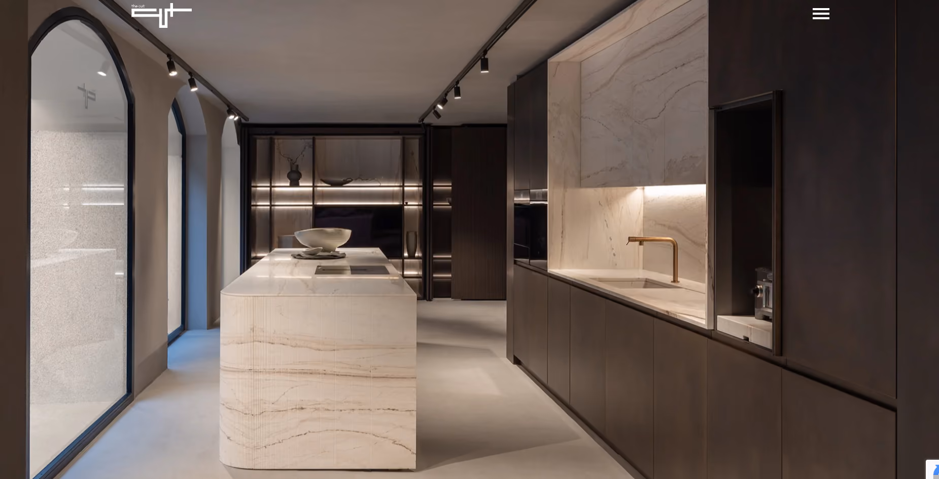 Modern kitchen with a large marble island in the center, dark wood cabinets, under-cabinet lighting, and three arched windows with black frames on the left.