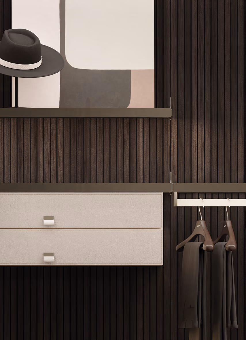 Modern closet with dark wood paneling, two beige drawers, hanging pants on wooden hangers, and a hat.