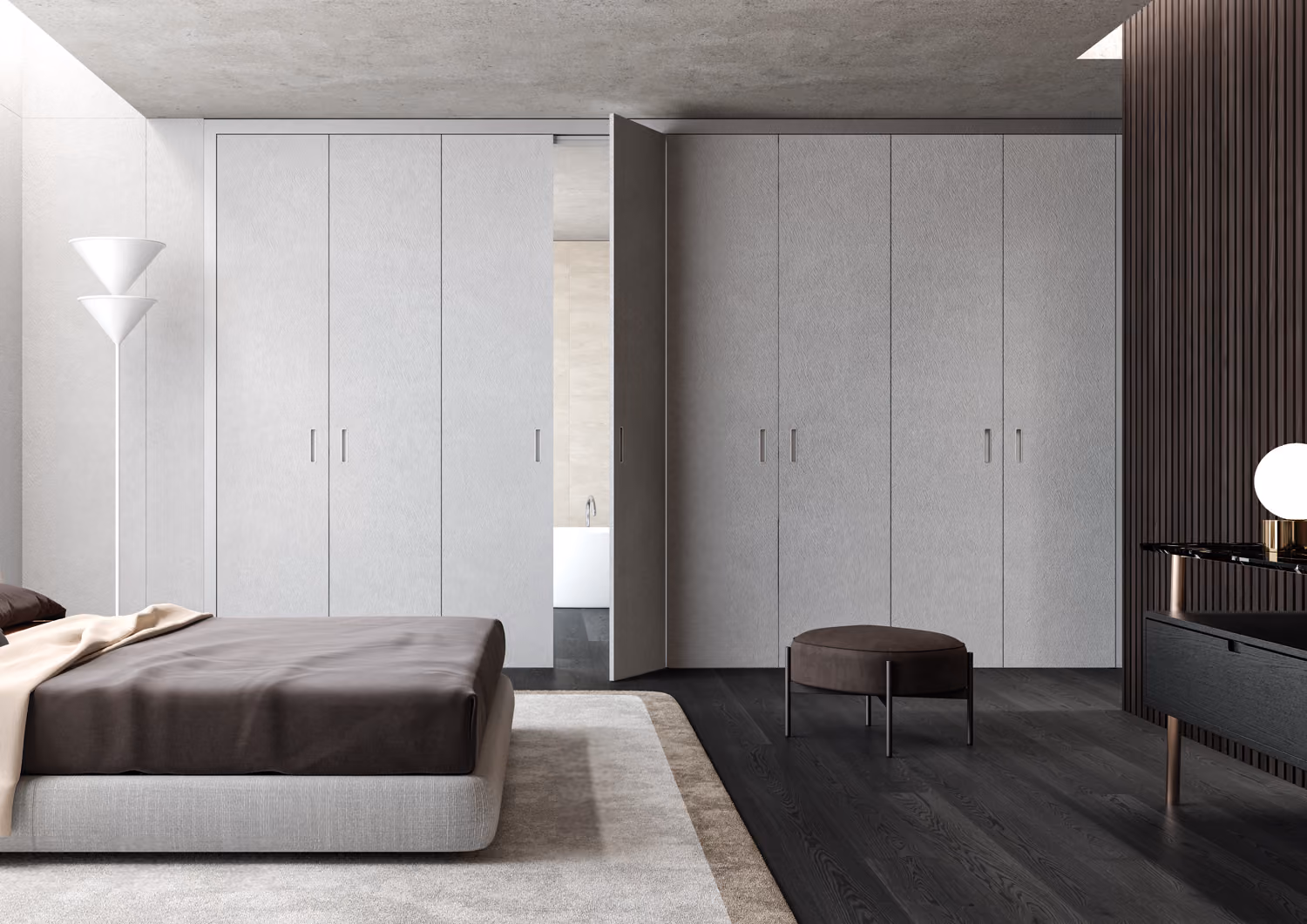 Modern bedroom with gray bed, white built-in closets, dark ottoman, and a glimpse of a bathroom.