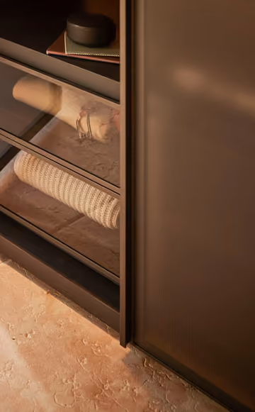 Modern brown cabinet with glass doors showing rolled white textured fabric inside.