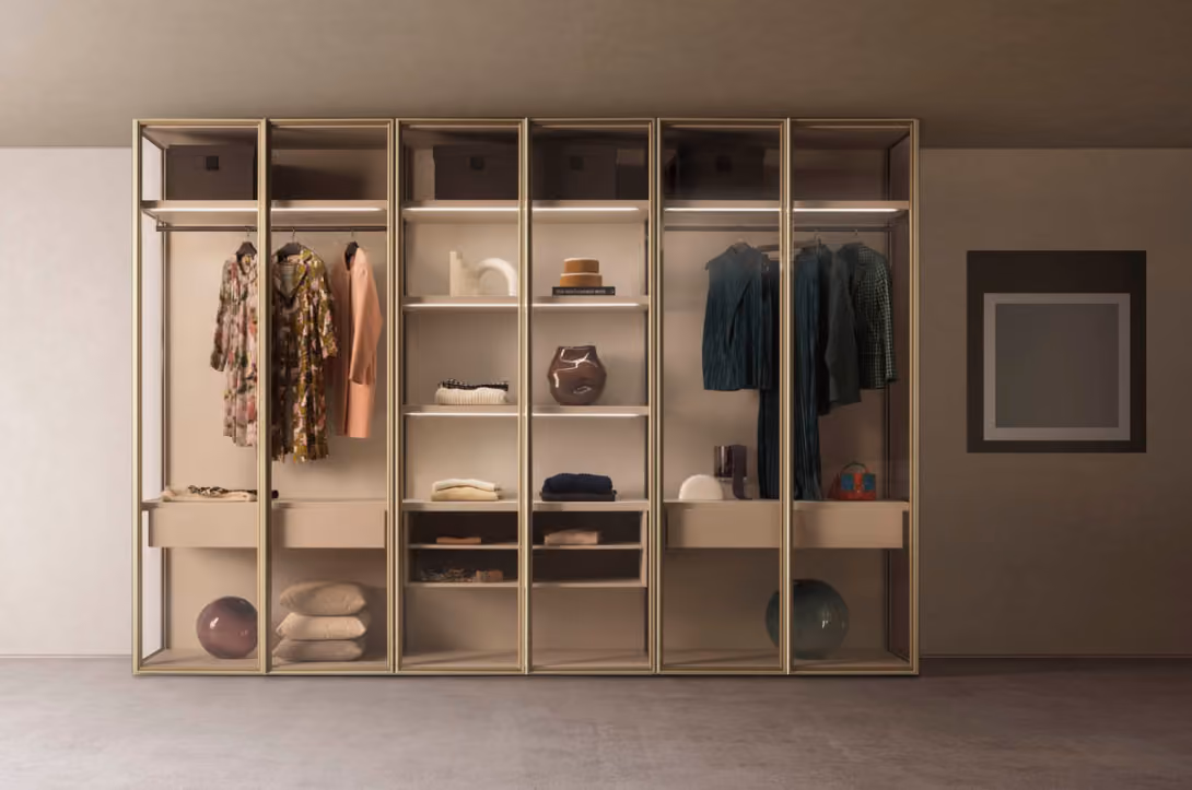 Modern wardrobe with glass doors showing dresses, sweaters, hats, boots, and decorative objects inside.
