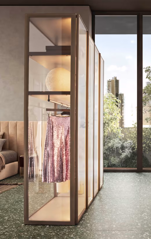Modern glass wardrobe with a sparkling pink skirt hanging inside in a bright room with large windows.