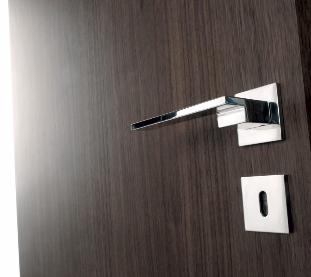 Modern chrome door handle on a dark wood door with a keyhole below.