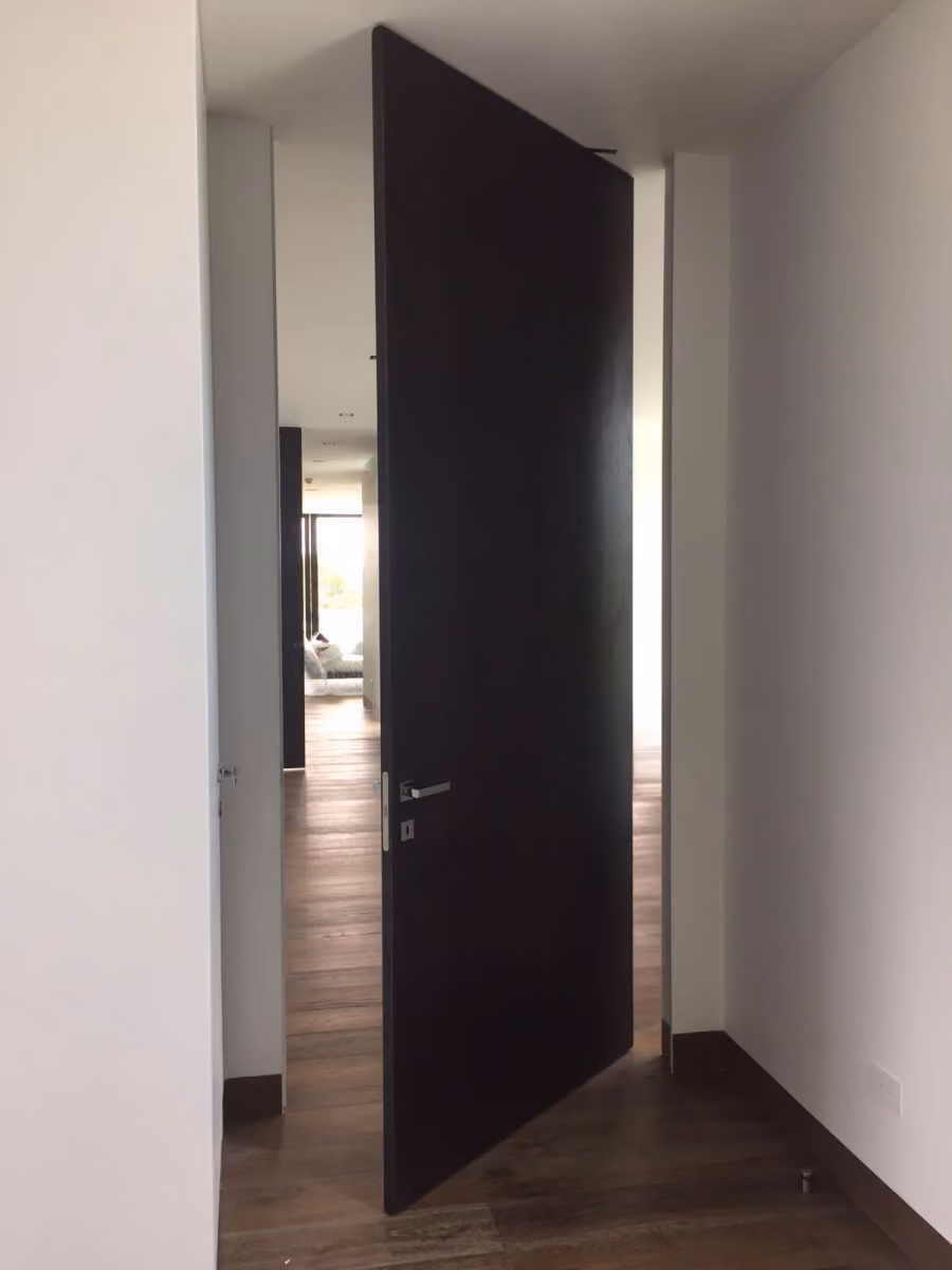 Dark wooden door slightly ajar in a hallway with wooden floors and white walls.
