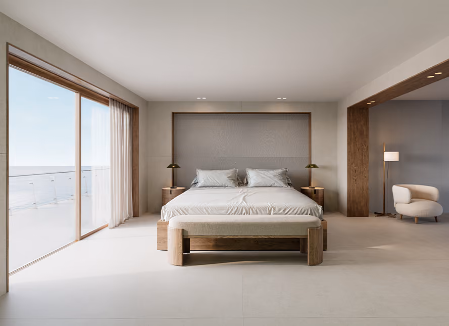 Minimalist modern bedroom with a large bed featuring two pillows and beige bedding, wooden nightstands with lamps, a wooden bench at the foot of the bed, floor-to-ceiling windows with sheer curtains showing a balcony and ocean view, and a white armchair with a floor lamp in an adjacent nook.