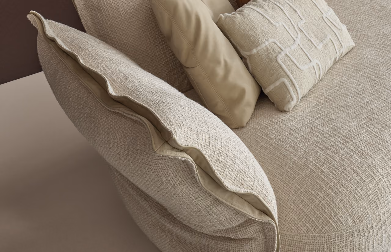 Close-up of a beige fabric sofa with three cushions in different textures and shades of cream and tan.