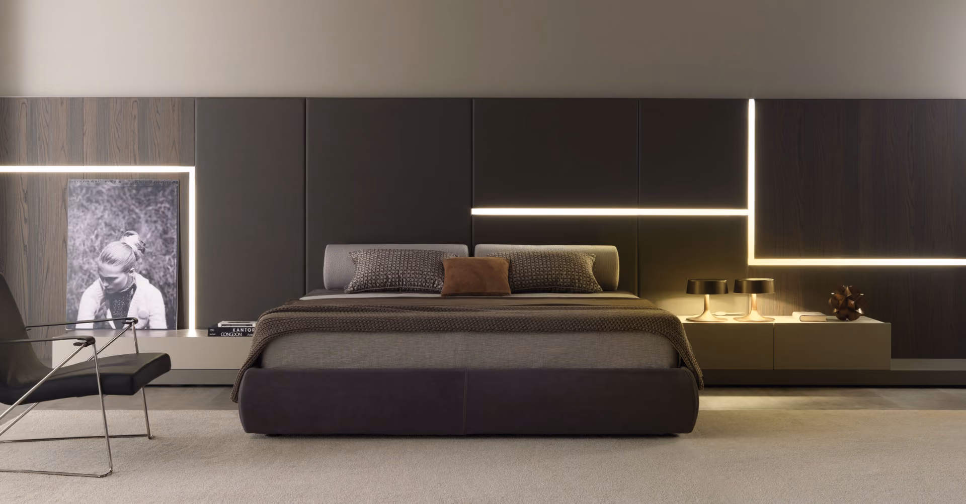 Modern bedroom with large upholstered bed in neutral tones, textured blankets, three pillows, sleek side tables with two black lamps, a decorative object, and a black and white portrait on a wood-paneled wall with integrated horizontal and vertical LED strip lighting.