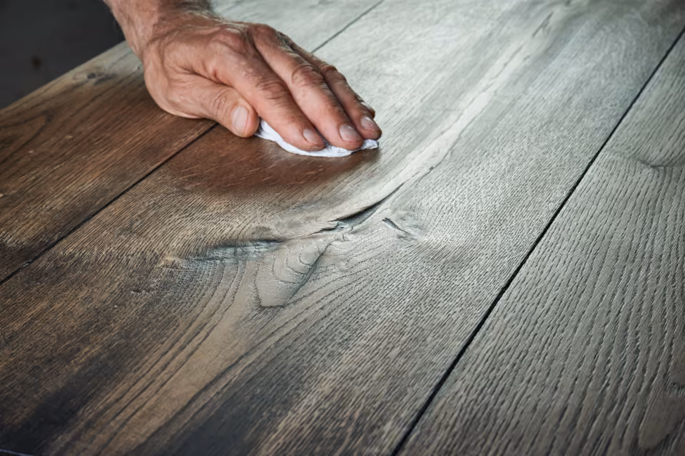 Close-up of a hand wiping and polishing a wooden surface with a white cloth, showing the wood grain and texture.