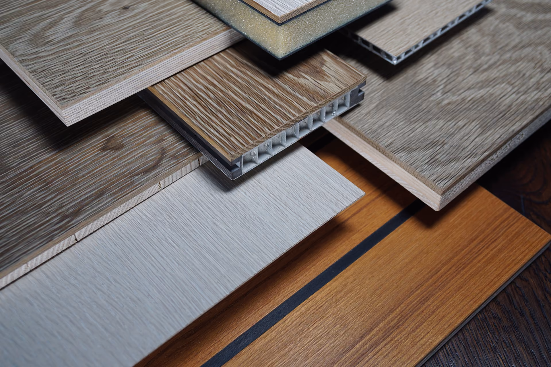 Close-up of various laminate and engineered wood flooring samples arranged overlapping, showcasing different wood grain textures, colors, and thicknesses.