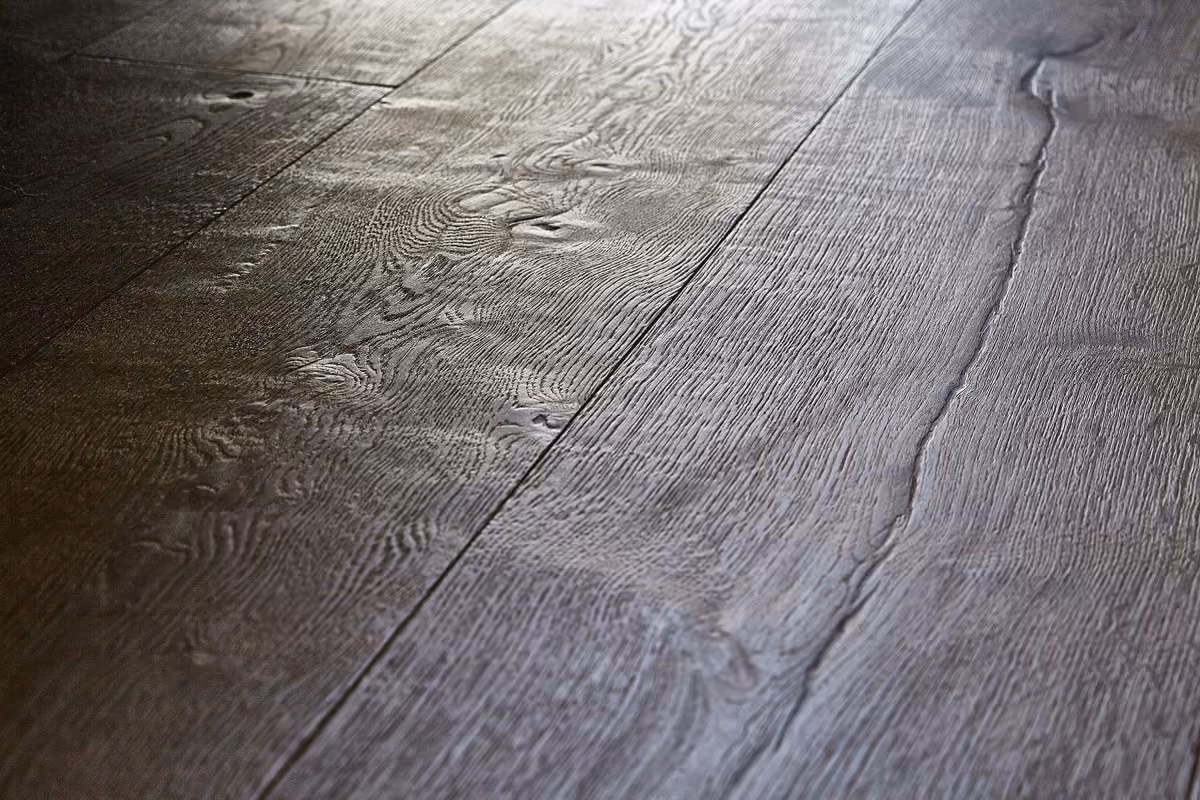 Close-up view of a textured dark wooden floor with visible grain and natural knots on the planks.