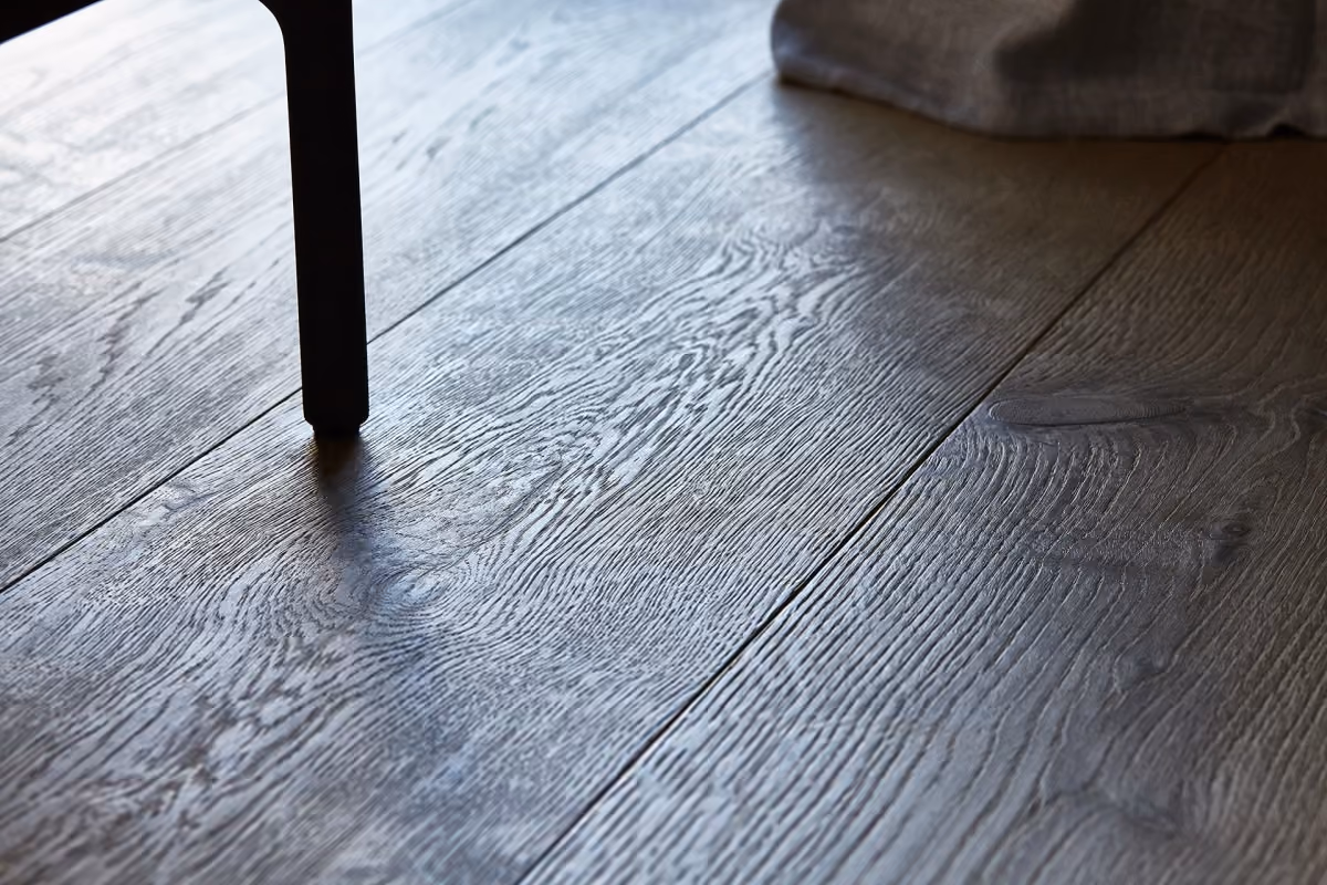 Dark wooden floor with visible grain and a single black chair leg casting a shadow.