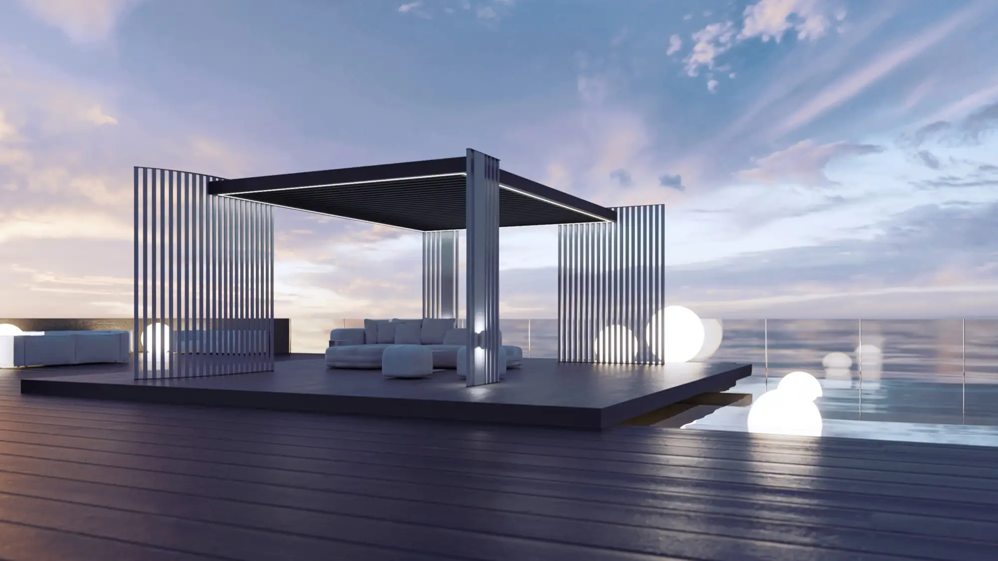 Modern outdoor lounge area with a raised dark platform featuring vertical slatted walls and a pergola-style roof, furnished with white cushioned seating, illuminated spherical lights placed around the deck, and a glass railing overlooking calm water at sunset under a partly cloudy sky.