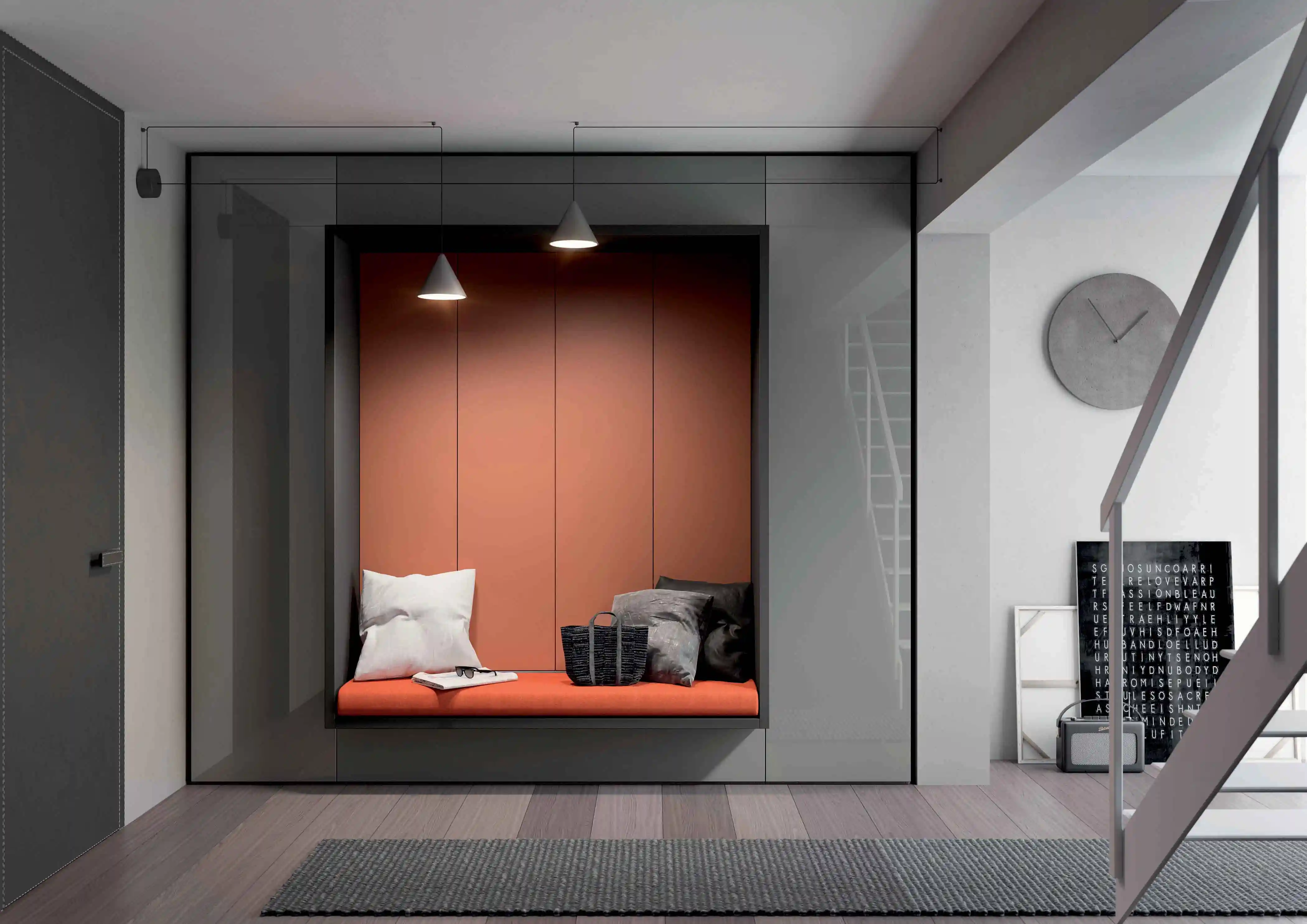 Modern interior with built-in seating niche featuring an orange cushioned bench, white and dark gray pillows, a black woven bag, and two pendant lights above, next to a wooden floor, gray rug, wall clock, and framed artwork leaning against the white wall near a staircase with gray railings.