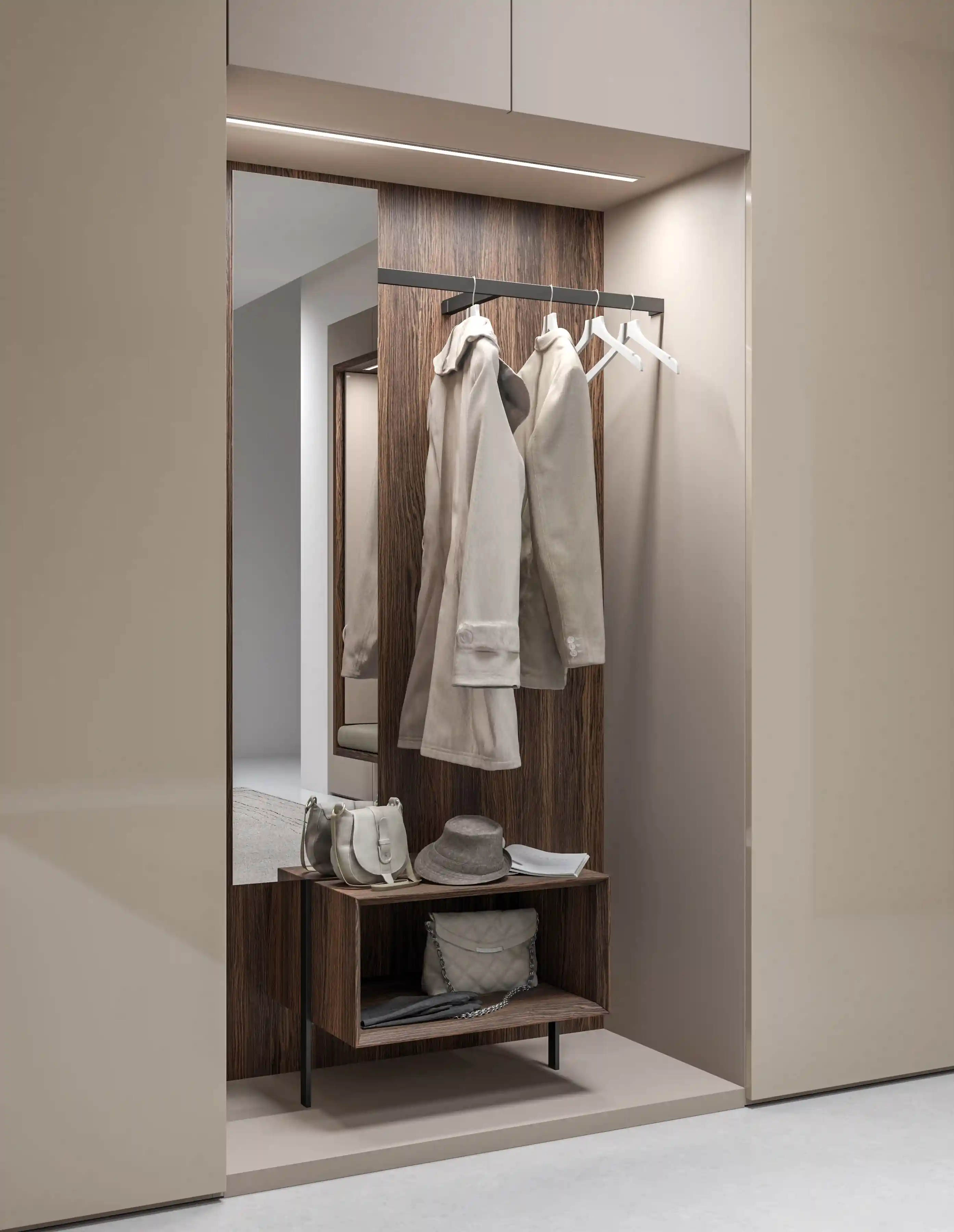Modern entryway closet with beige walls featuring a wood panel backdrop with a black metal rod holding two beige coats and three empty white hangers, a tall rectangular mirror on the left, and a wood shelf below holding a grey hat, two beige handbags, and an umbrella.