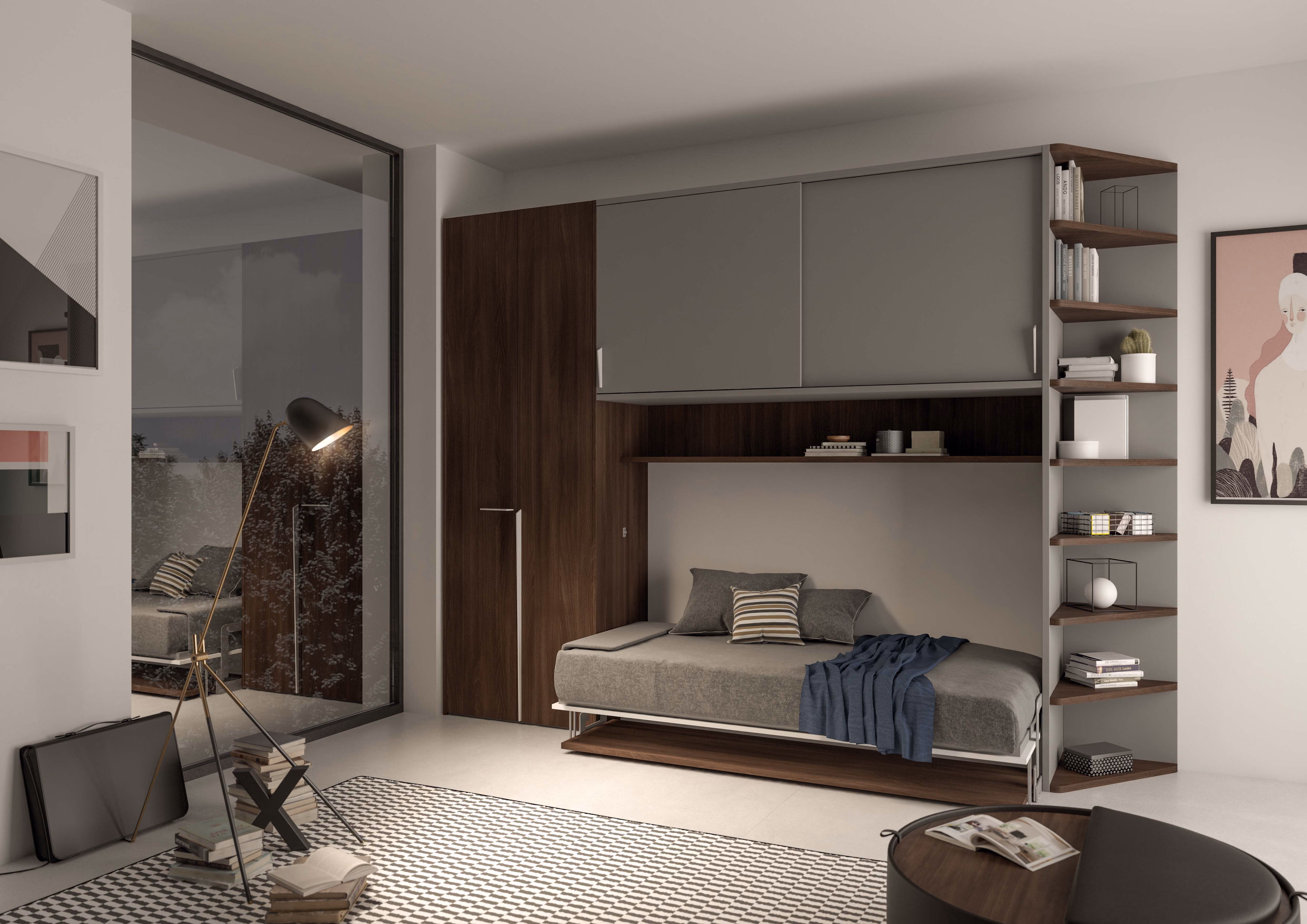 Modern bedroom featuring a gray daybed with pillows and a blue throw under wooden overhead storage cabinets, next to a floor lamp and corner shelving unit with books and decor, on a checkered rug and light floor.