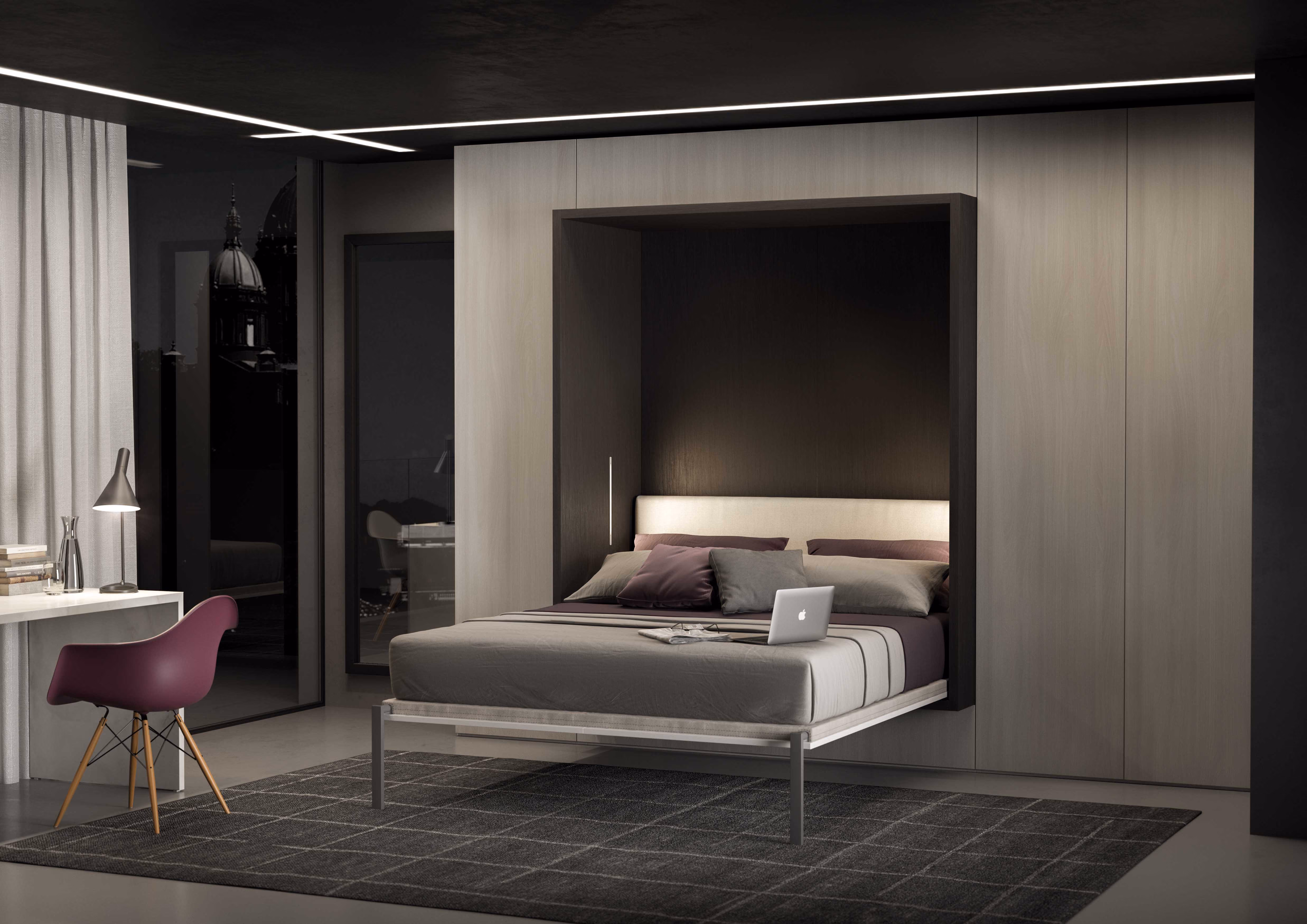Modern bedroom with a wall-mounted fold-down bed featuring gray bedding, a laptop, and pillows, set against a sleek black and beige wall background, with a purple chair near a white desk with books and a lamp, and a large gray patterned rug on the floor.