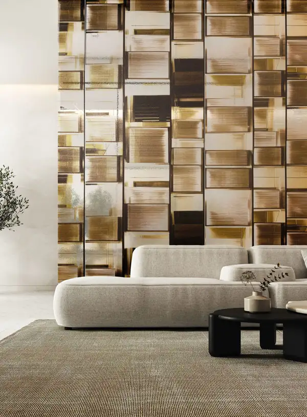 Modern living room with a large, curved light beige sofa on a textured rug, black round coffee tables holding minimalistic vases, and a wall decorated with vertical panels of reflective, abstract gold and bronze geometric patterns.