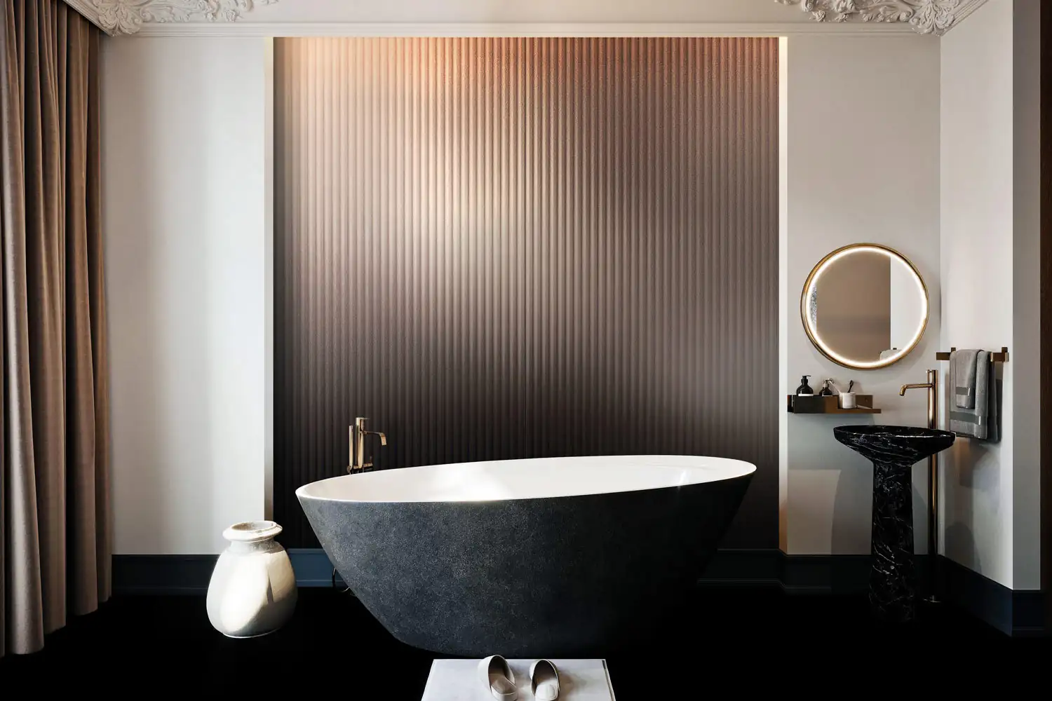 Modern bathroom with a large freestanding black and white bathtub in front of a vertically ridged gradient wall, a black marble pedestal sink with a round illuminated mirror, and a pair of slippers placed on a small rectangular platform.