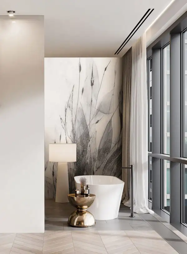 Modern bathroom with a white freestanding bathtub positioned near large floor-to-ceiling windows with sheer white curtains, a tall white lamp, and a metallic gold side table holding toiletries, set against a wall featuring large-scale abstract floral artwork in shades of gray.