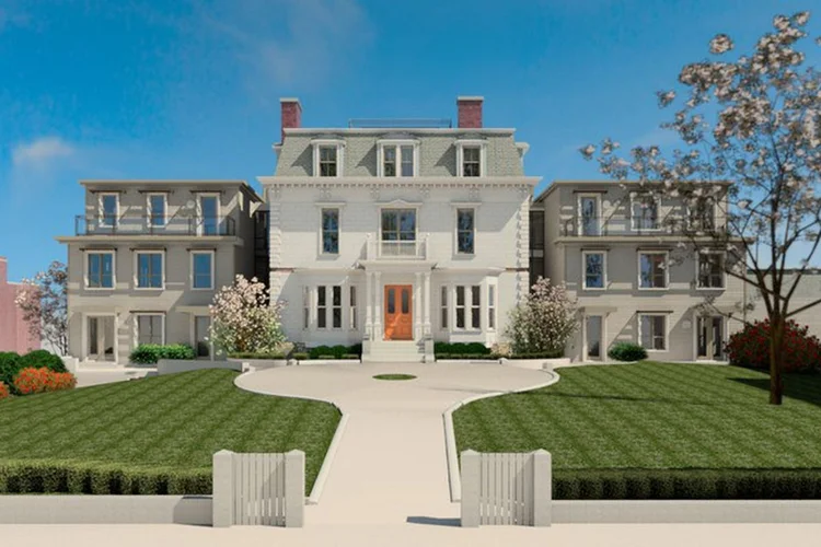 Large white mansion with three stories, symmetrical design, two chimneys, and an orange double front door, surrounded by landscaped green lawns, bushes, and blossoming trees under a clear blue sky.