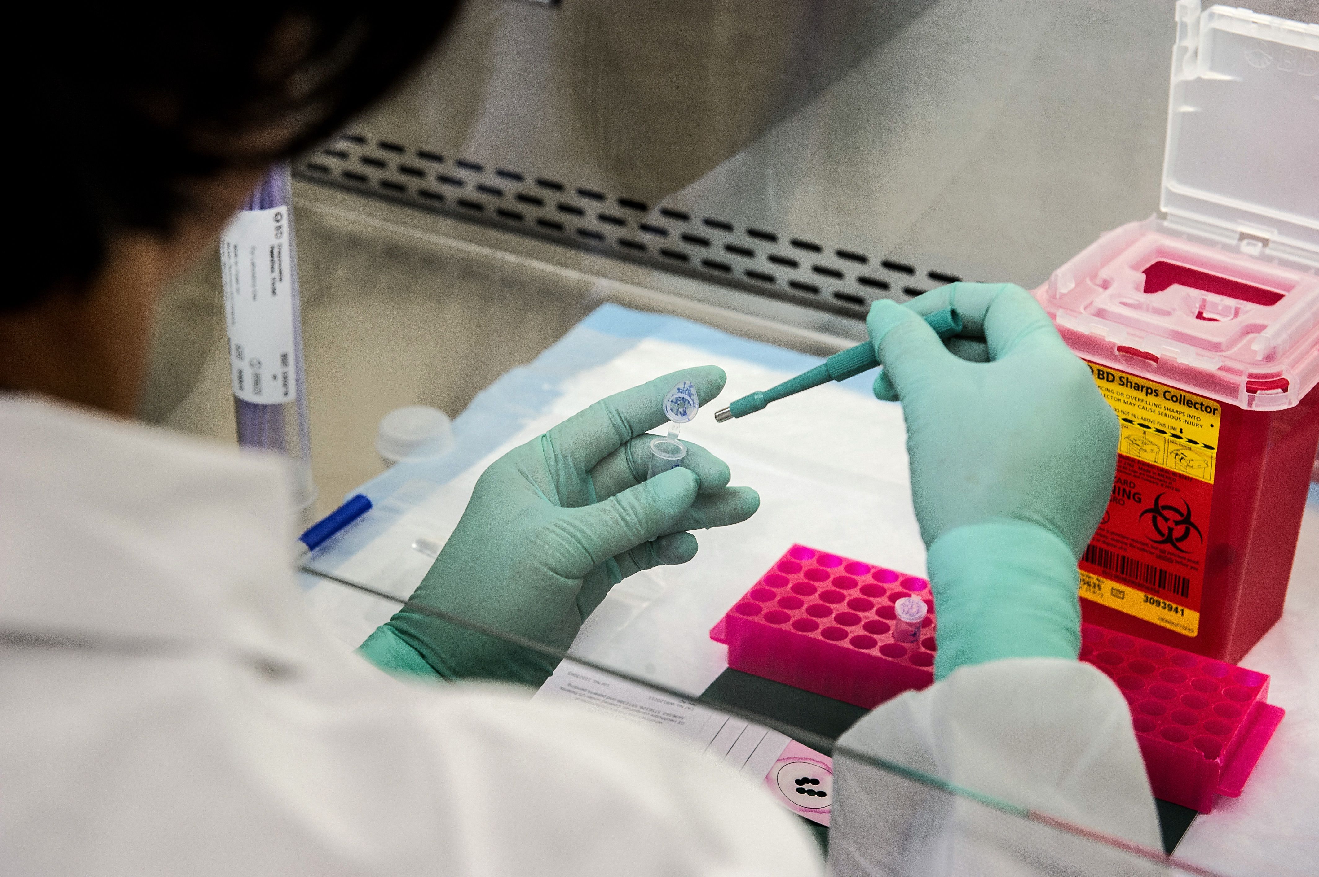 A lab technician in a white coat and nitrile gloves pipetting a cannabis concentrate sample into a test vial inside a clean-room testing lab.