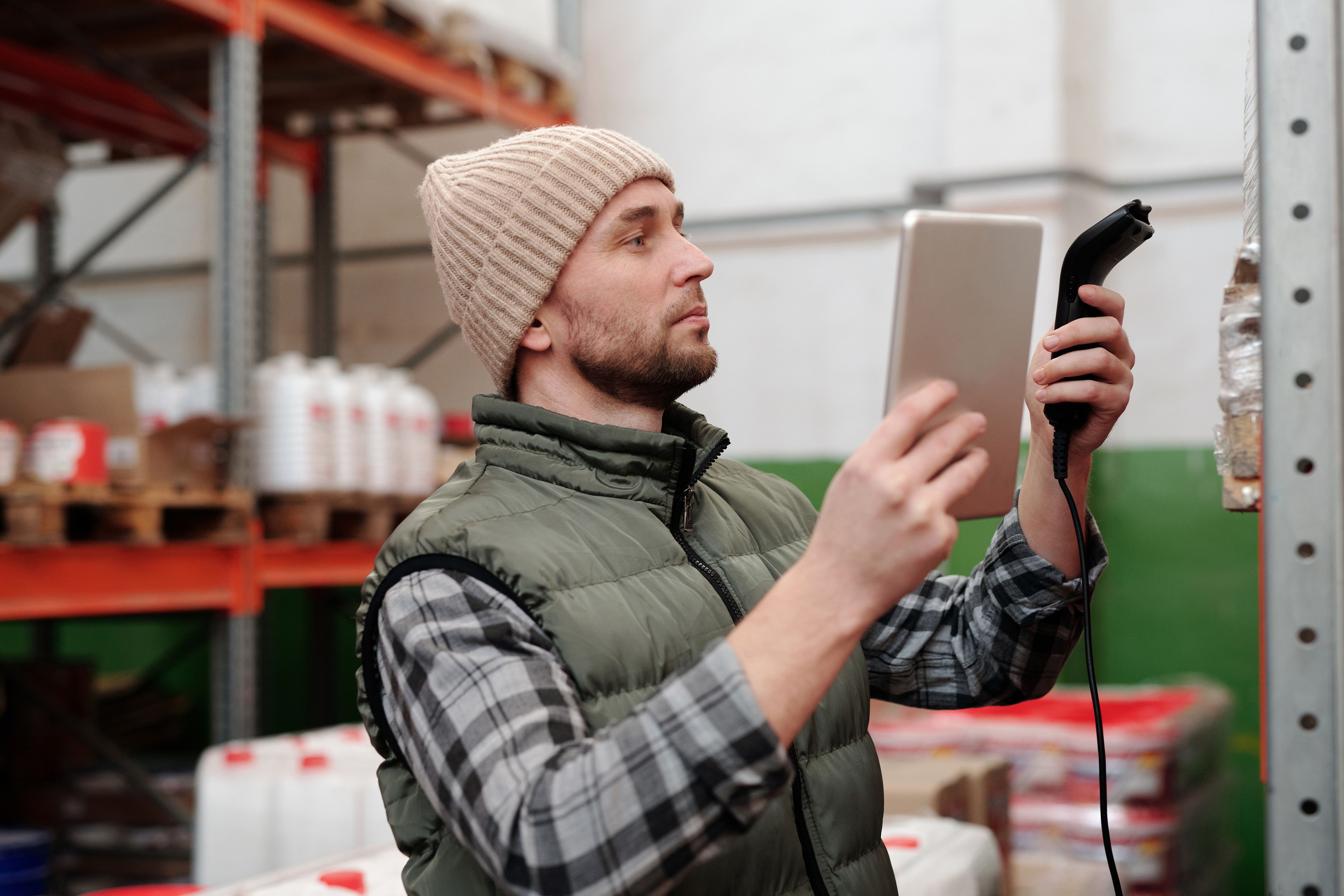 A worker logging inventory counts on a handheld scanner while standing next to shelves of labeled cannabis product bins.