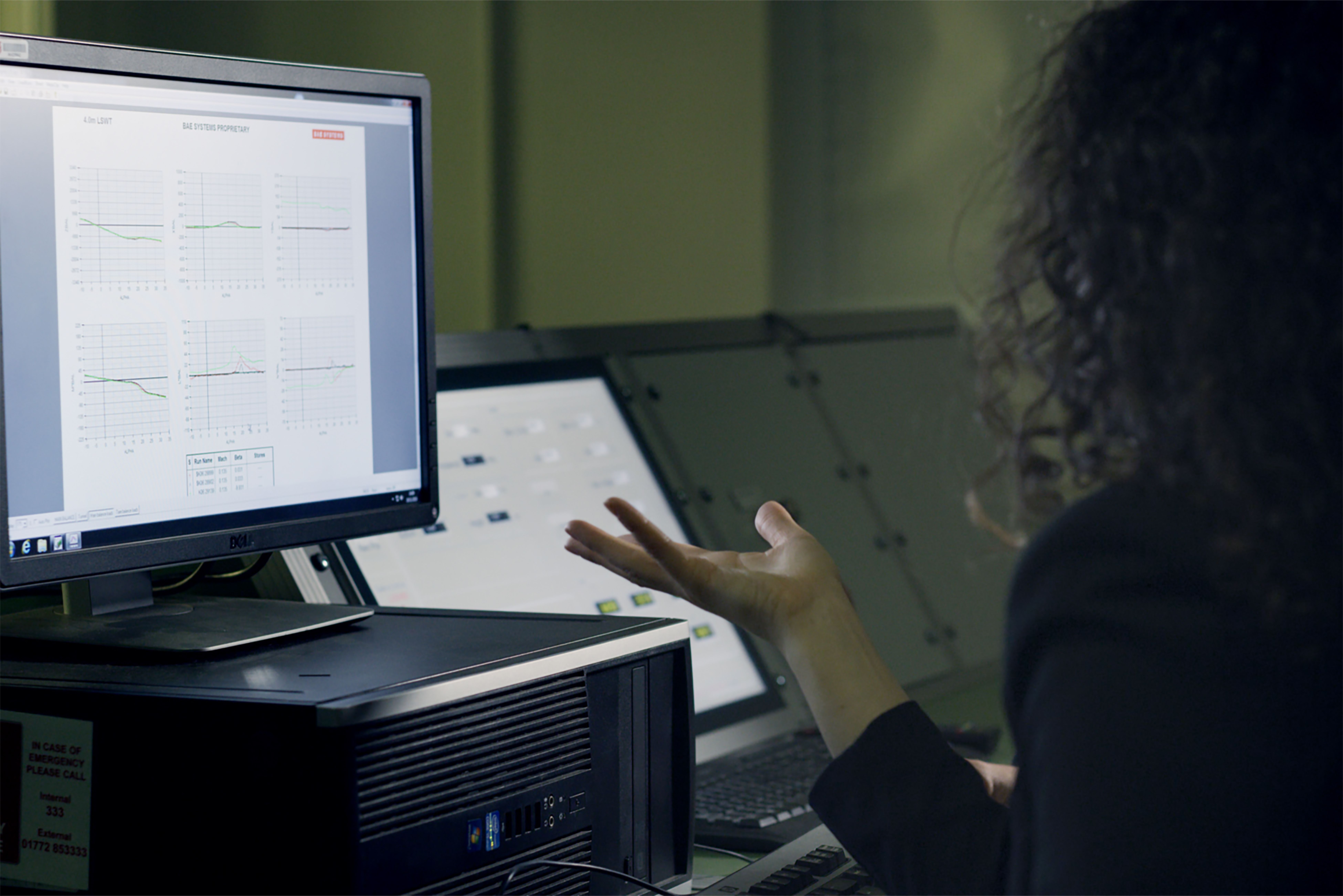 Visual input: A desk with three monitors, one showing a maintenance forecast chart, one showing a document, and one showing a live production dashboard.