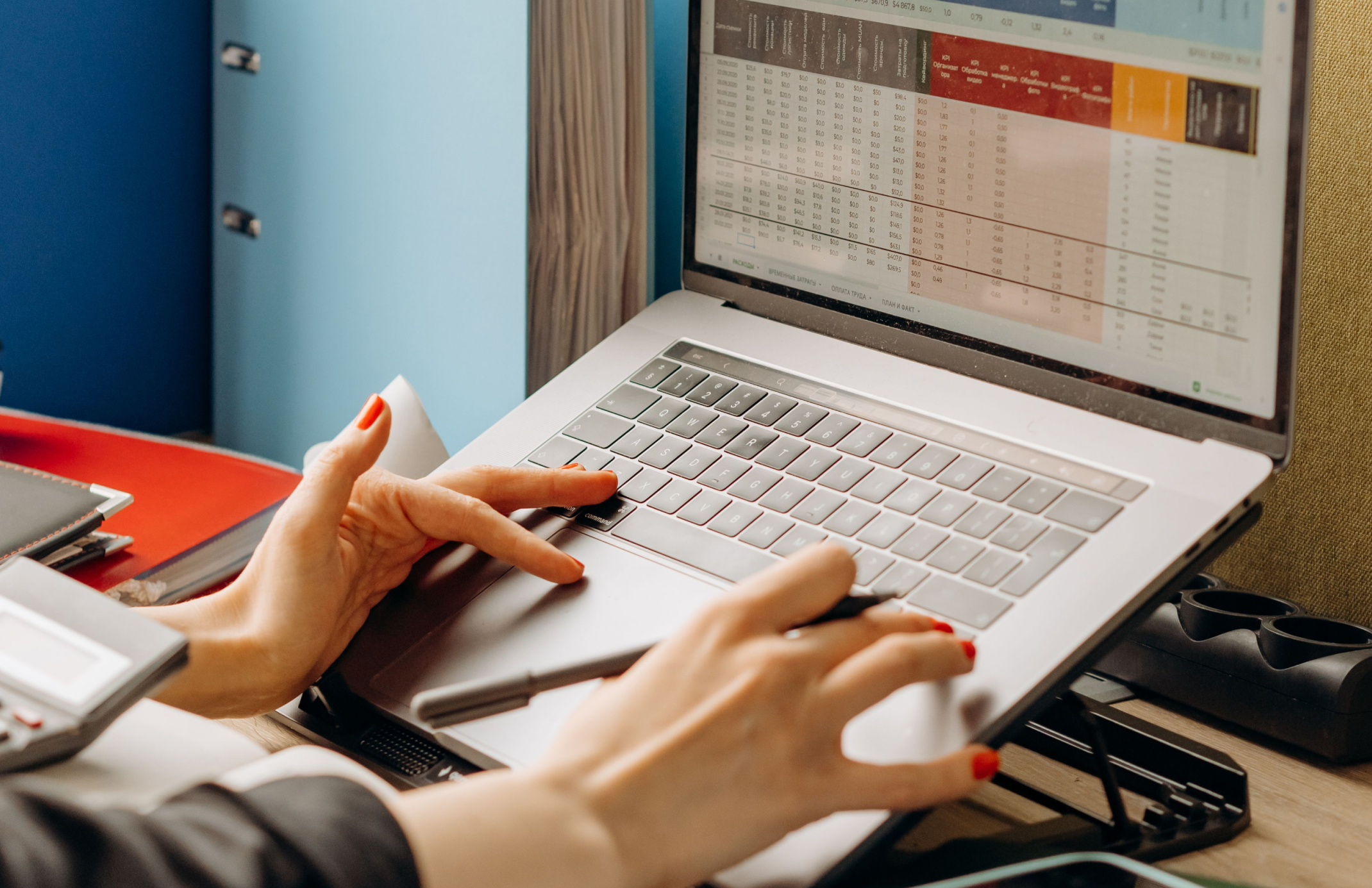 A desk, two monitors — one showing a spreadsheet, one showing an ERP dashboard.