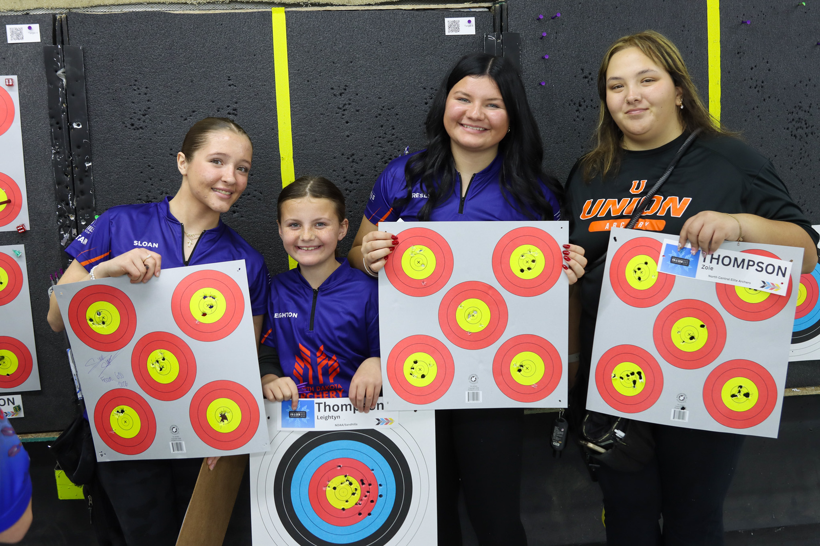 Four young archers holding target faces with tight arrow groupings