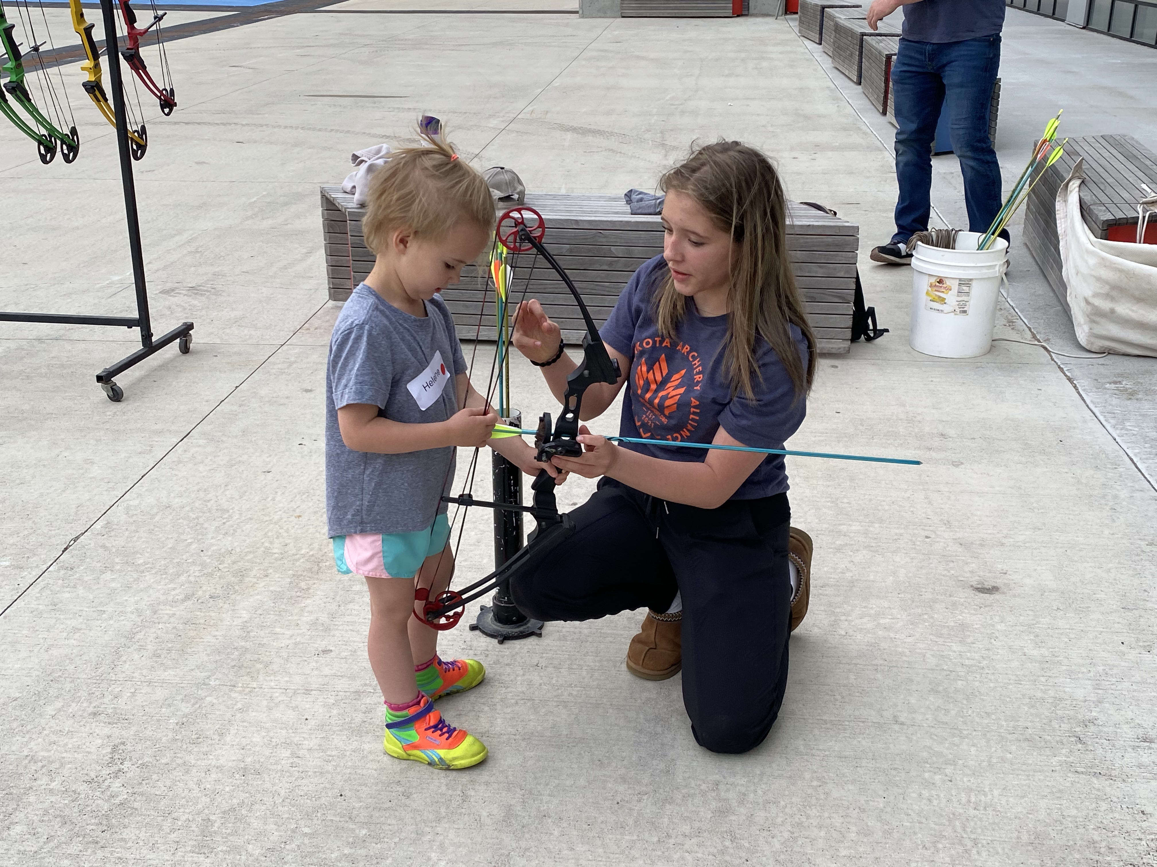 Coach helping a young girl adjust a compound bow at an indoor archery range