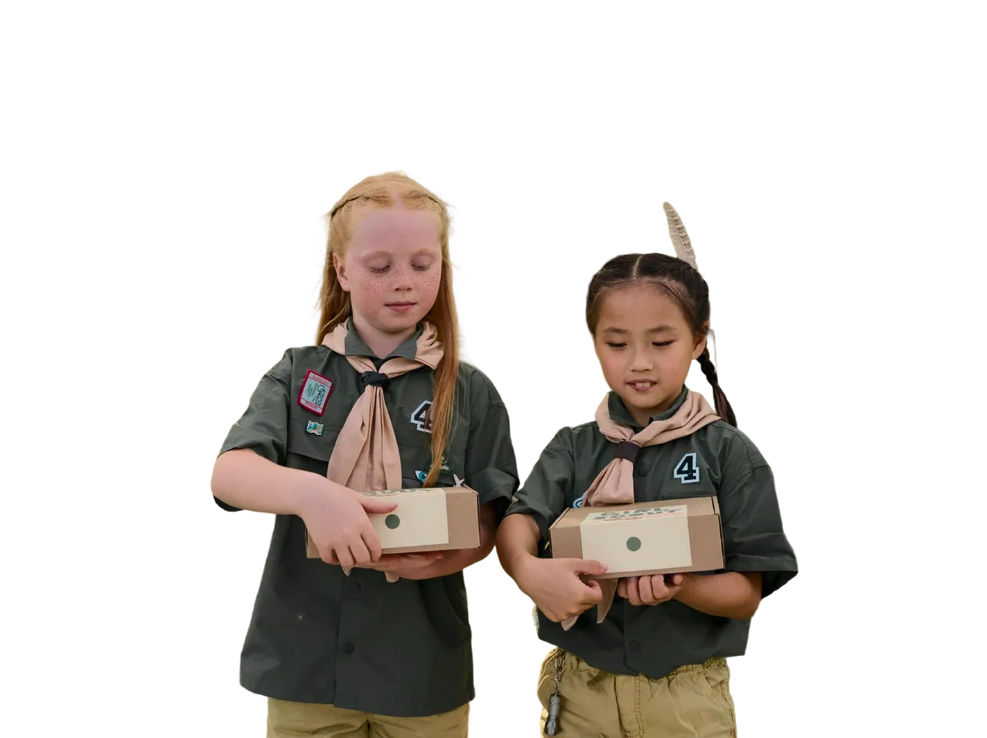 Two young girls in scout uniforms holding small cardboard boxes, one with a feather in her hair.
