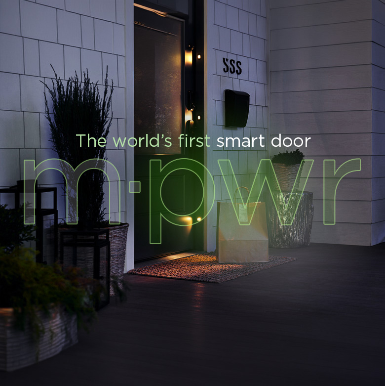 Evening view of a modern house entrance with a black front door illuminated by warm lighting, surrounded by plants in decorative pots, and the text 'The world’s first smart door m-pwr' overlaid.