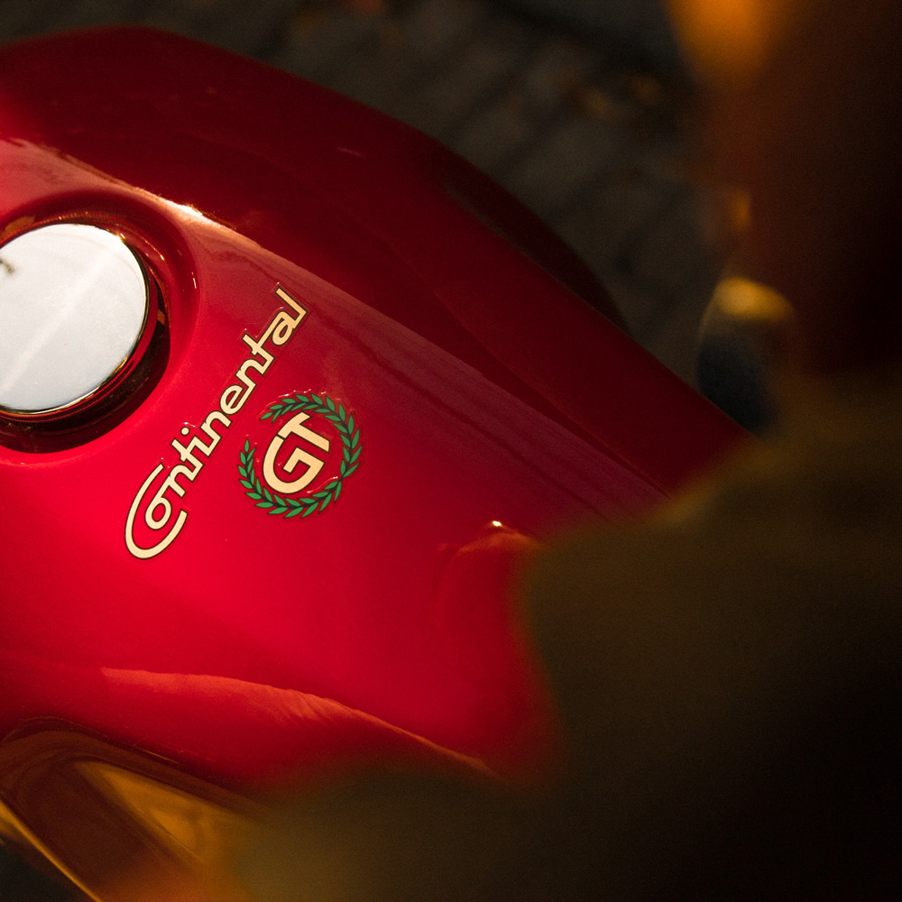 Close-up of a shiny red motorcycle fuel tank with the word Continental and a GT emblem surrounded by a green laurel wreath.