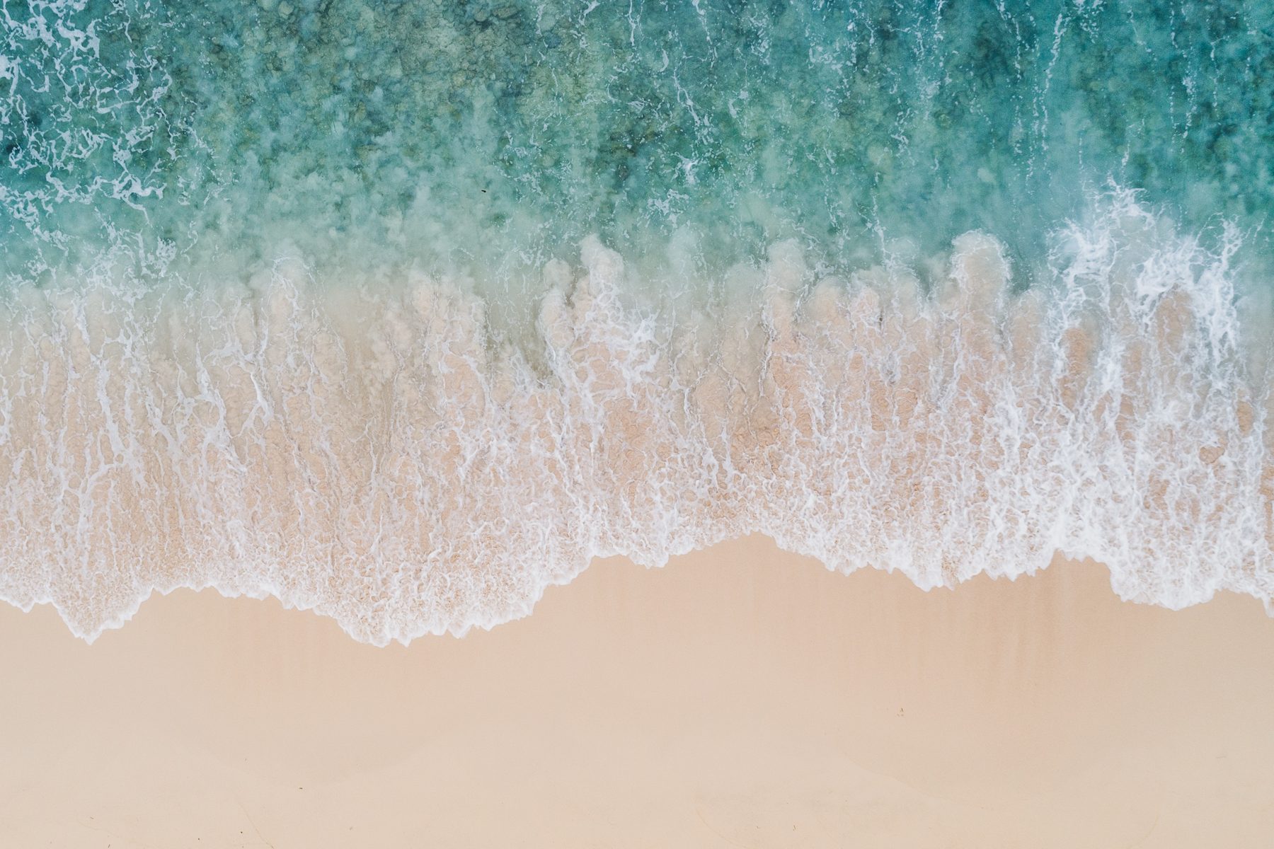 Aerial view of turquoise waves washing onto a sandy beach