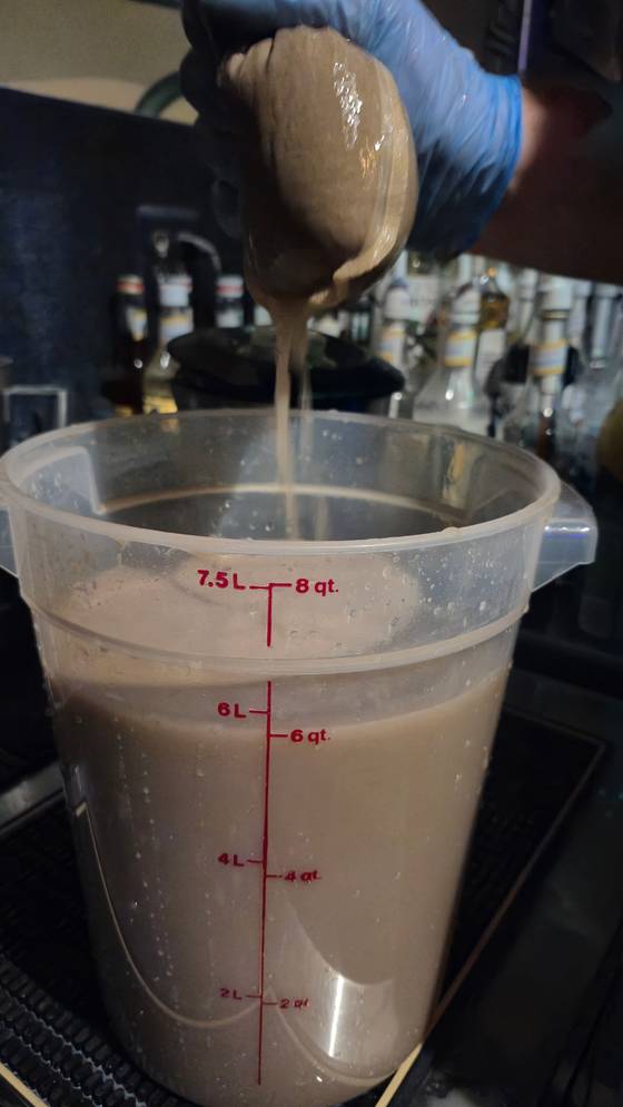 Spent kava marc squeezed through a straining bag into a graduated food-service container