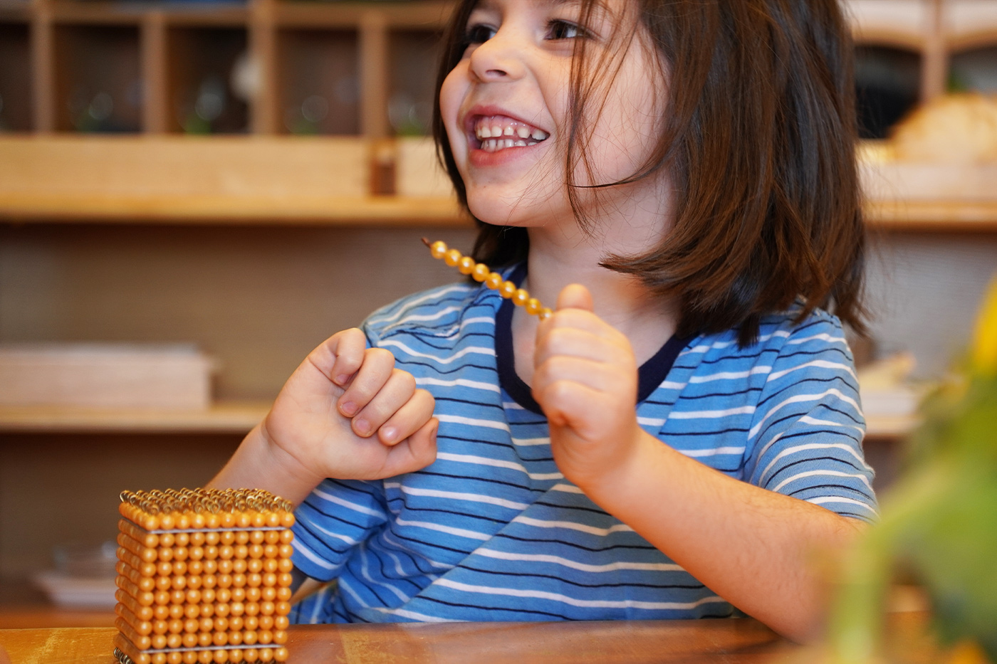Student in Battery Park Montessori classroom smiling and working with counting beads
