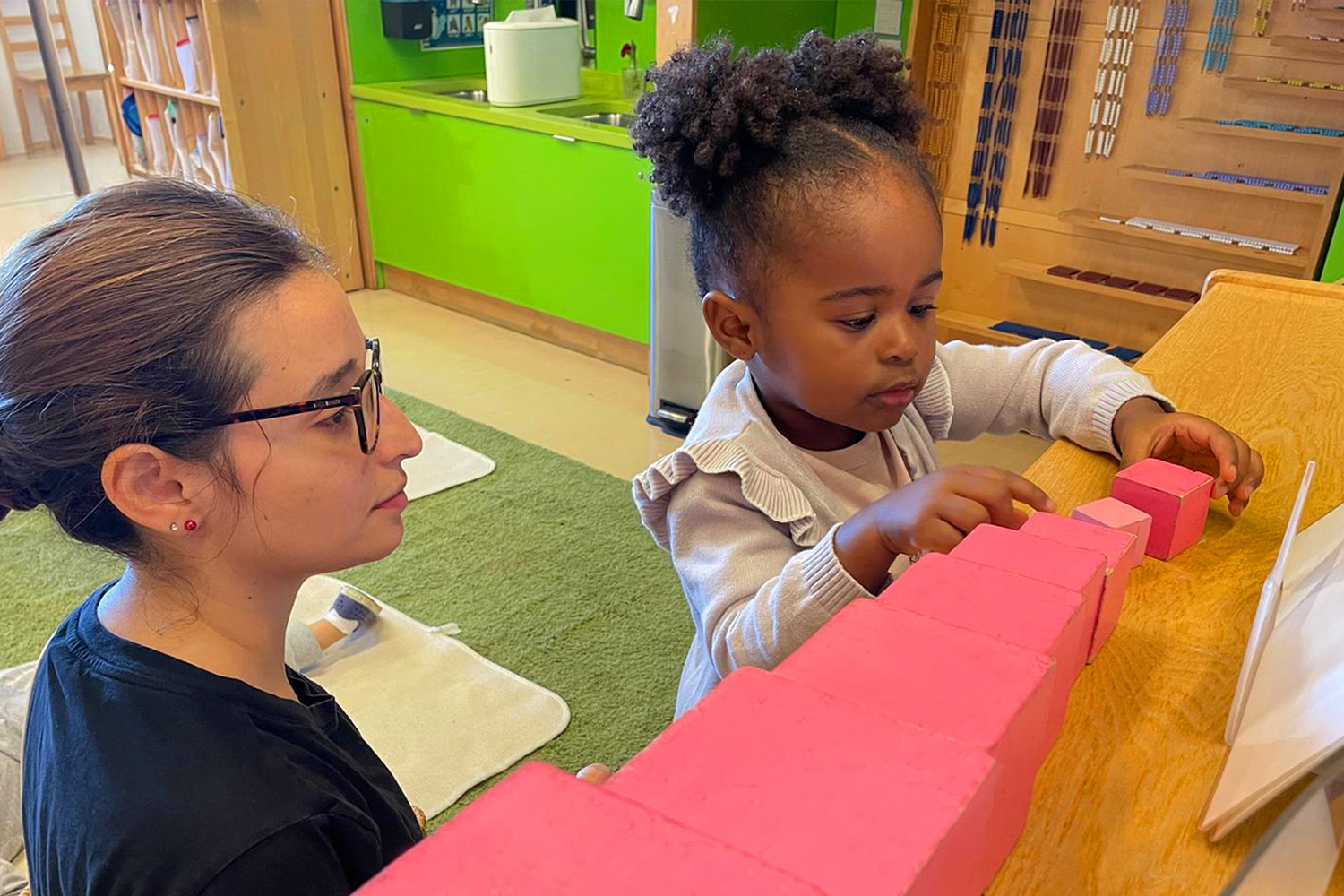 Battery Park Montessori student works with Montessori blocks as teacher observes in classroom